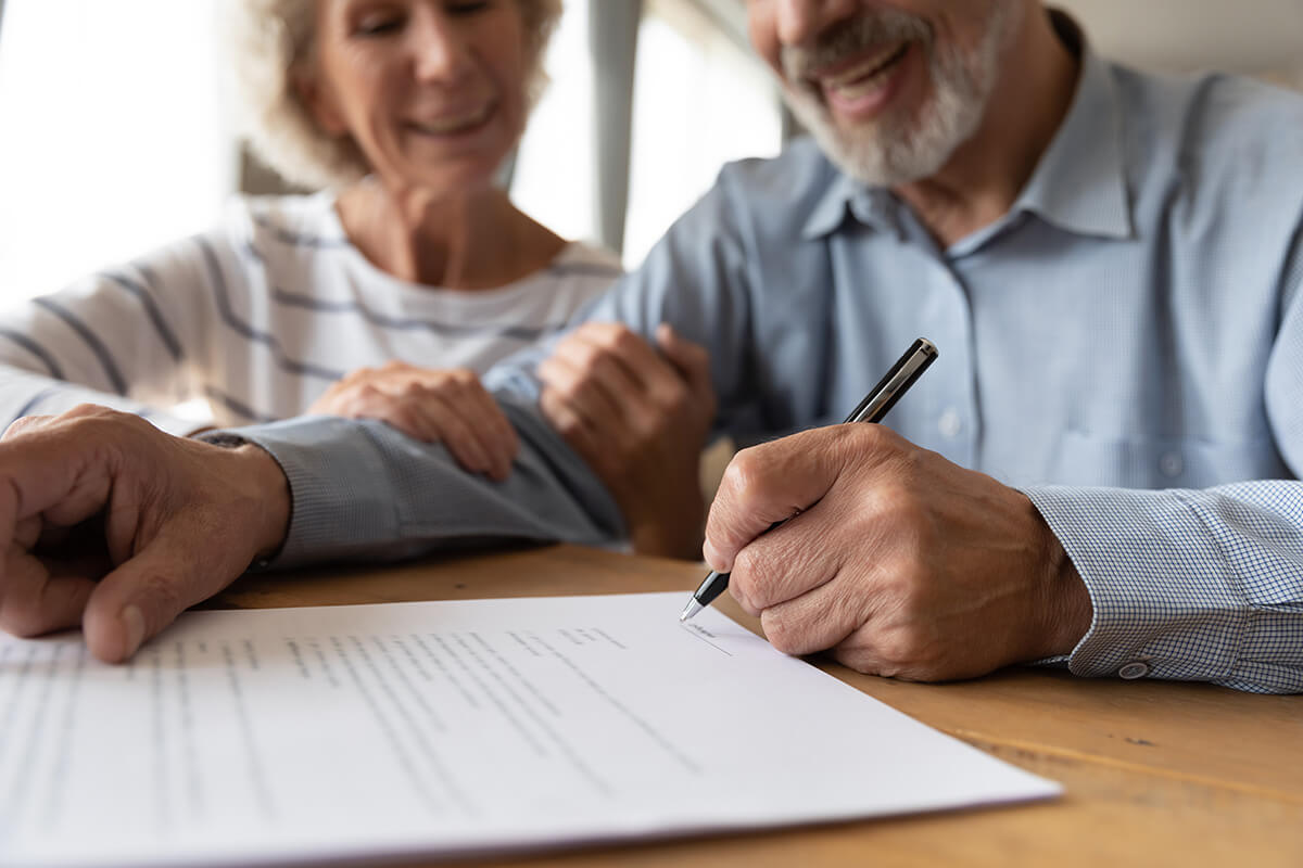 husband and wife sit at desk sign health insurance contract
